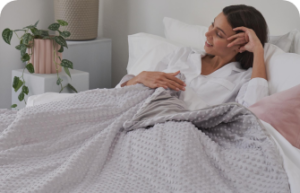 Woman smiling in her bed, under a grey weighted blanket