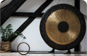 A black and gold gong hanging in front of some wooden beams and a plant